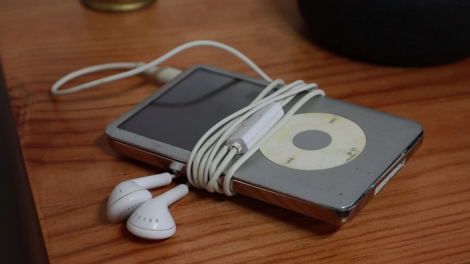Reproductor con audífonos de cable enrollados, en primer plano, sobre una mesa de madera.
